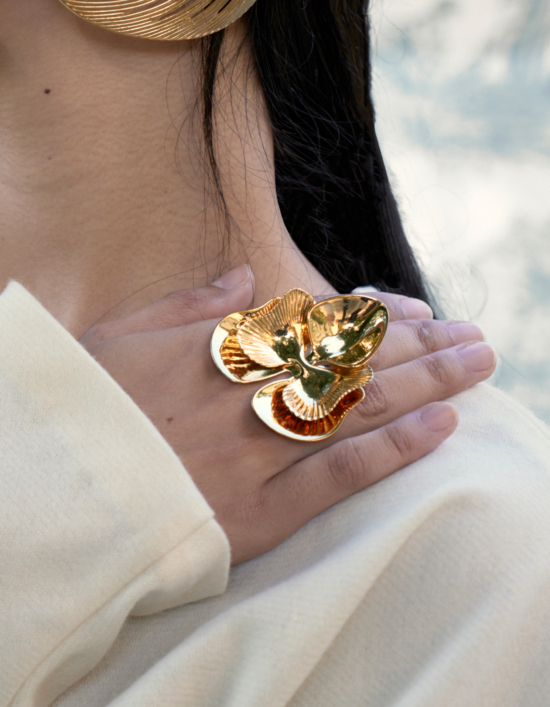 Close-up of a hand wearing the FLOA Design gold-plated Orchid Ring (large), showcasing its intricate floral design and reflective surface.