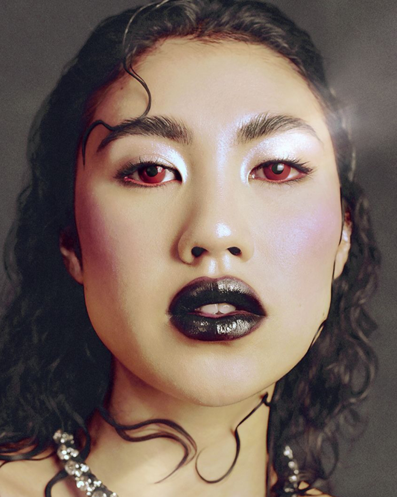Model with dark feminine energy makeup, featuring black lipstick, shimmering eyeshadow, and red eyeliner.