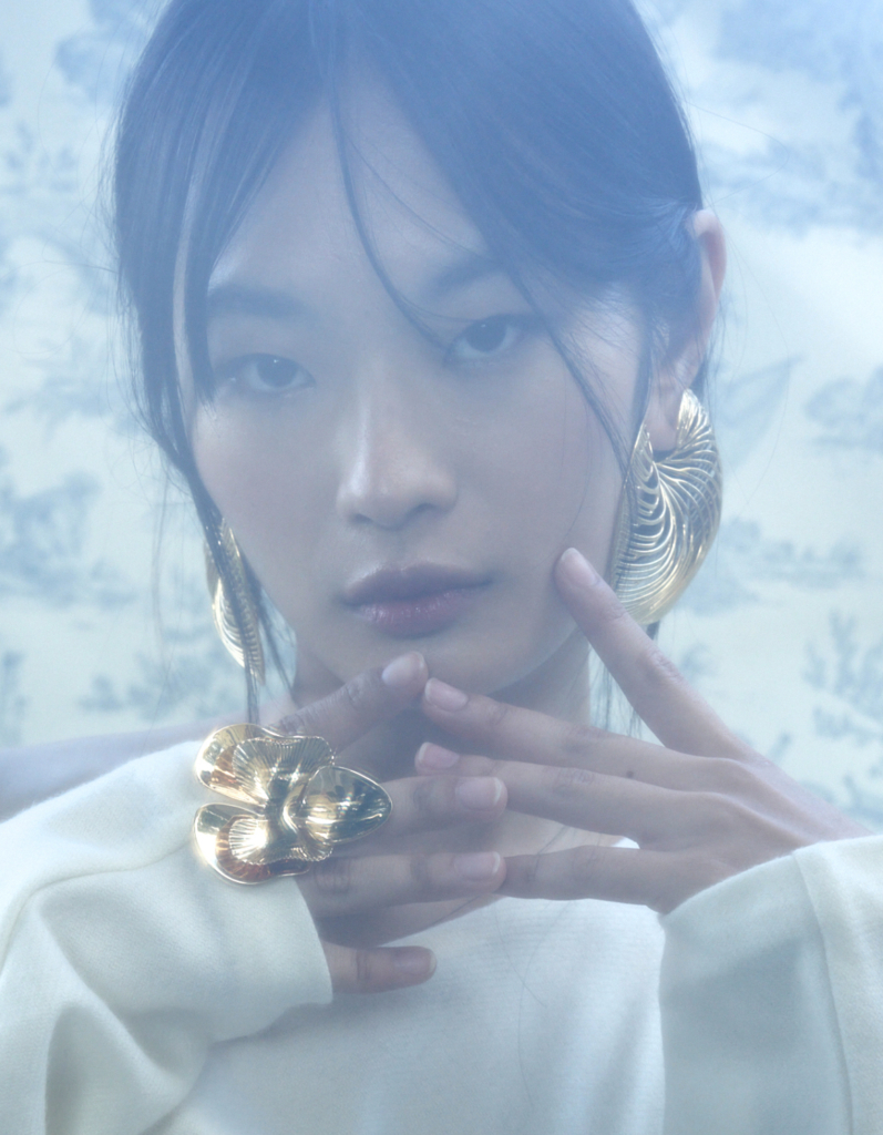 Portrait of a model wearing FLOA Design jewelry, featuring the gold-plated Argonaut Shell Earrings and large Orchid Ring, captured in a soft, ethereal light.