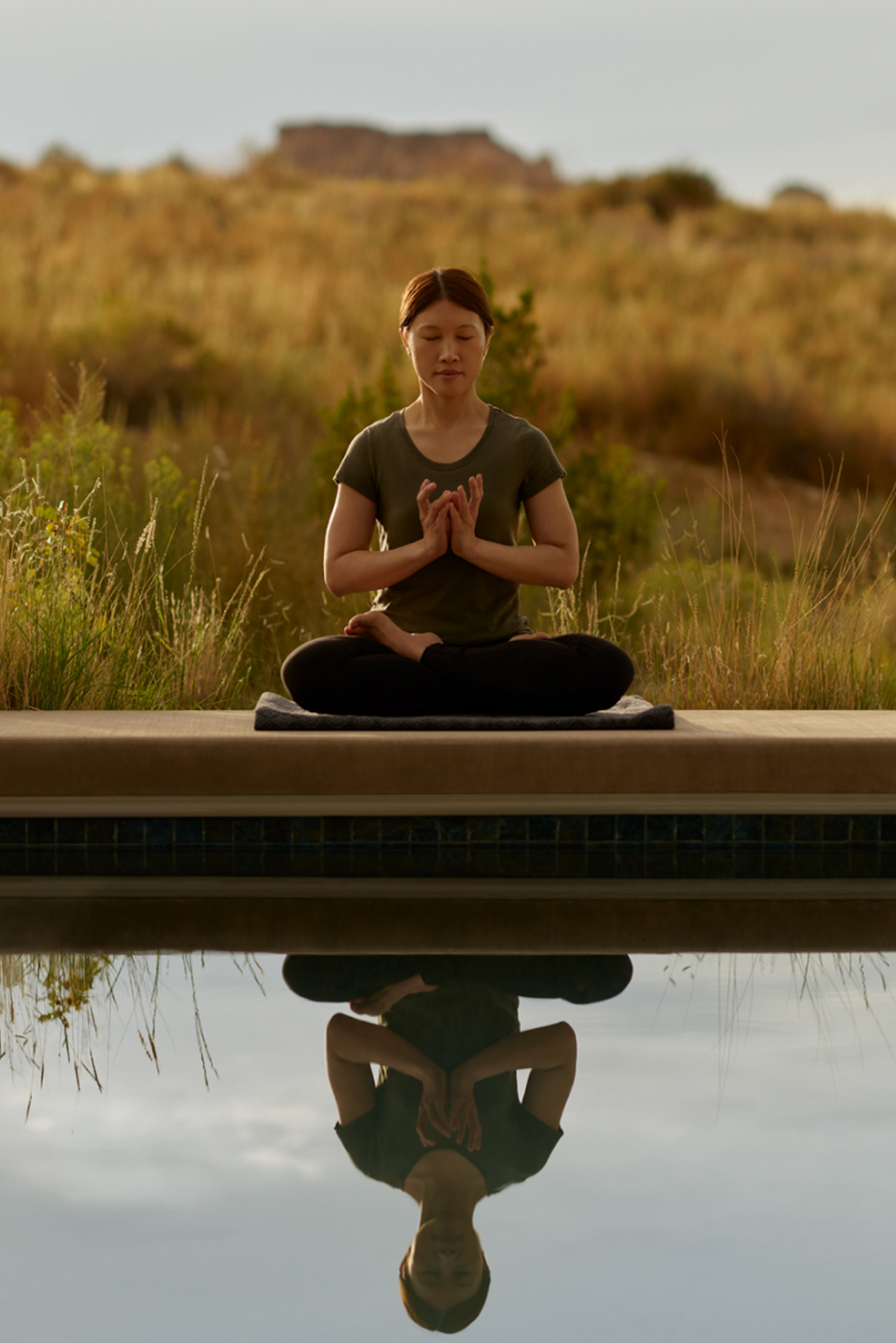 Woman meditating outdoors in lotus pose with reflection in water